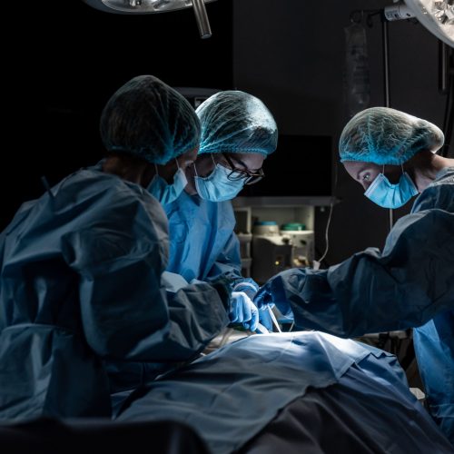 Diverse group of male and female surgeons in operating theatre wearing face masks performing surgery. medicine, health and healthcare services during coronavirus covid 19 pandemic.