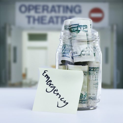 Shot of a note reading Emergency against a jar filled with money on a hospital counter.